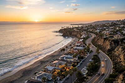 High-altitude aerial view of the Orange County coastline at sunset, Pacific Coast Highway curving along the bluffs