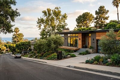 Modern coastal California hillside home with partial ocean view in the distance, tree-lined residential street